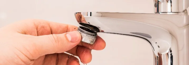 Hand nimmt verkalkten Perlator aus Wasserhahn